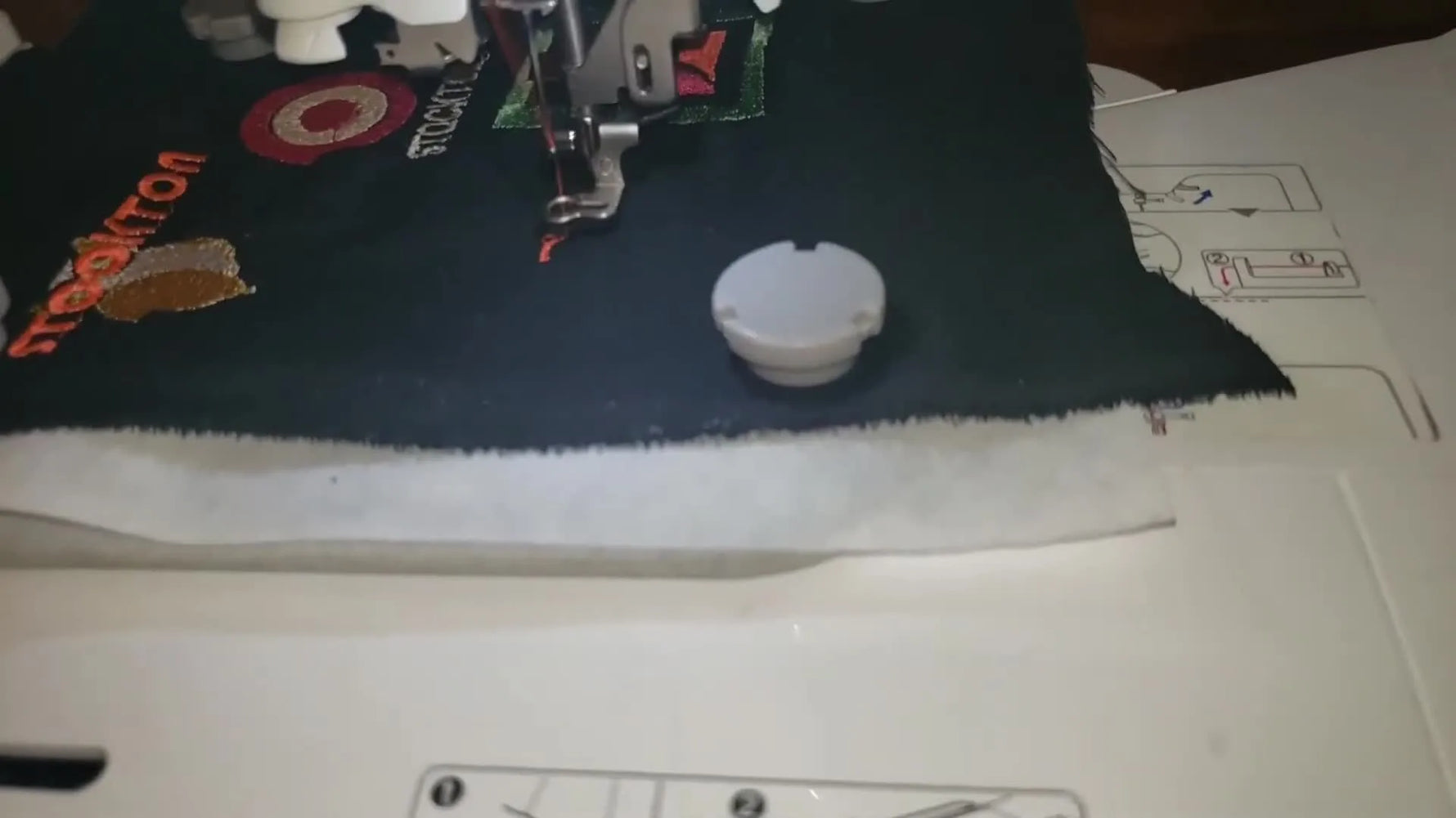 A Brother PE535 stitches a red monogram on black fabric while two small magnets hold the fabric in place over a hooped stabilizer.