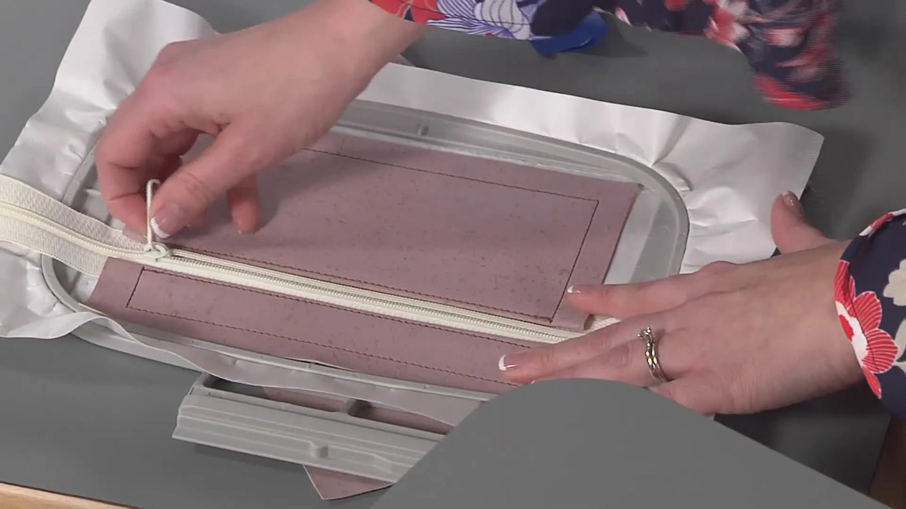 Hands opening the zipper halfway inside the hoop—an essential step that prevents an ITH pouch from getting trapped and unturnable.