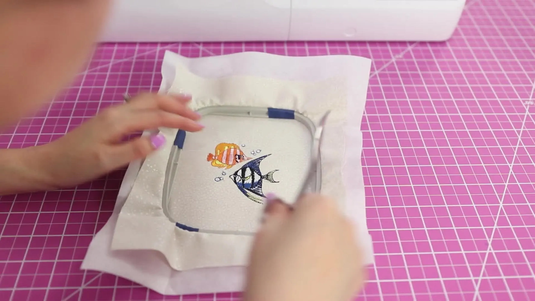 A close-up of the finished multi-color fish embroidery stitched cleanly on white fabric in the hoop.