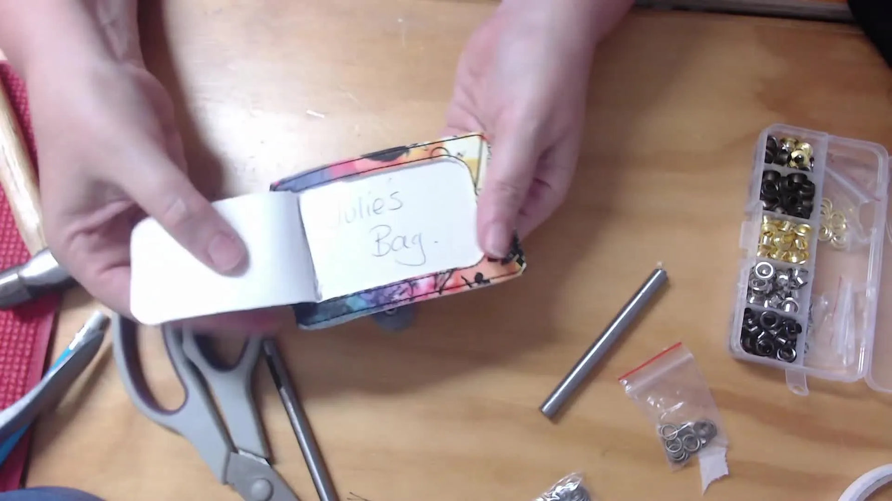 A finished in-the-hoop vinyl luggage tag is held open to show a business-card-sized insert behind a clear window and a neatly set metal eyelet.