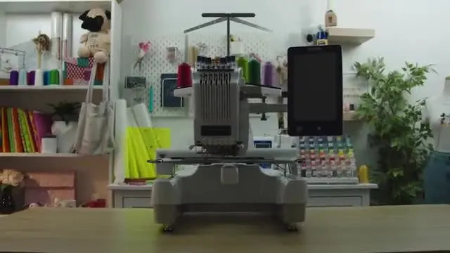 A full front view of the Brother PR670E set up on a workbench with thread spools and the large touchscreen ready for embroidery.
