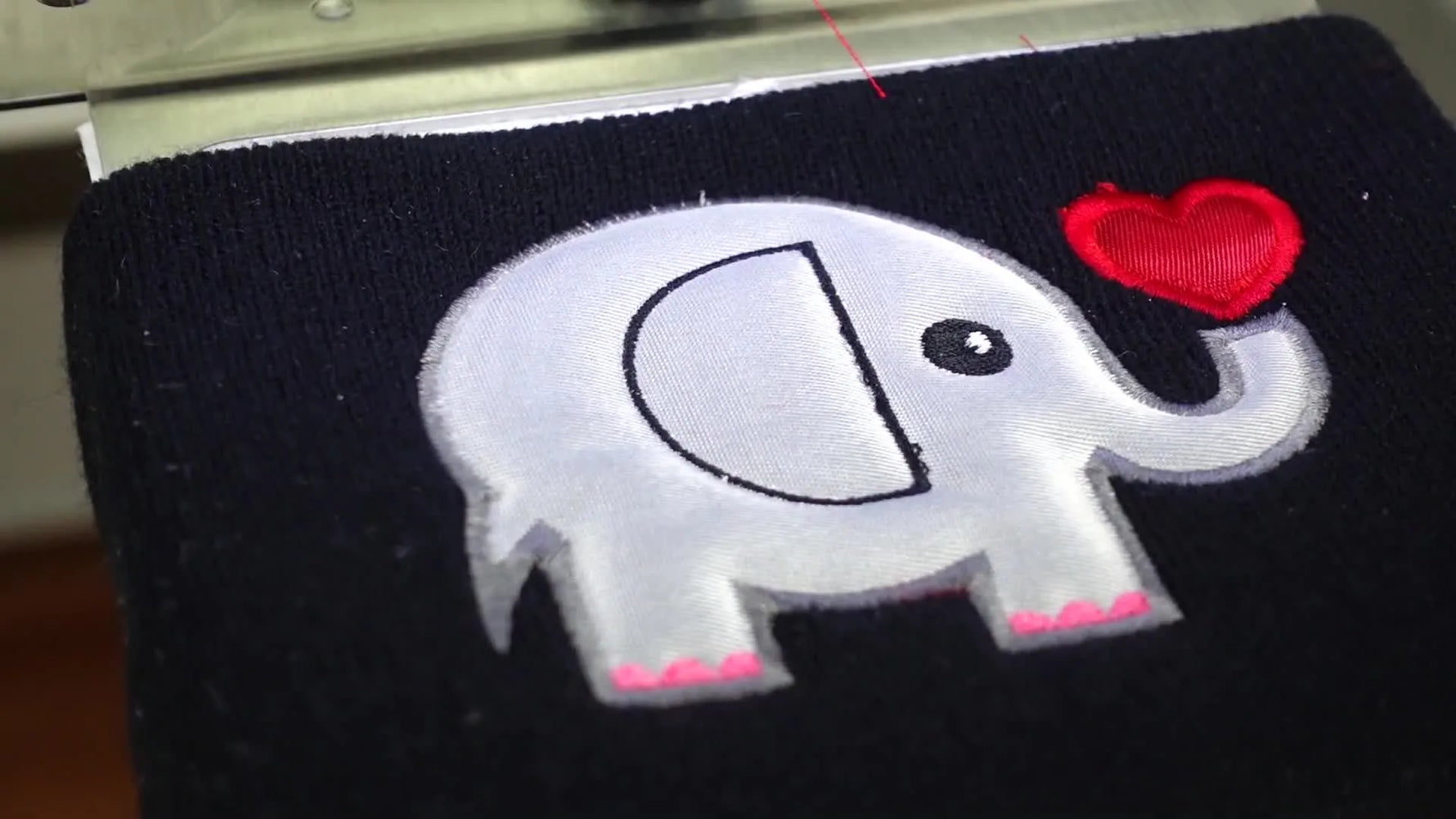 A close-up of the finished elephant appliqué stitched cleanly on a black knit beanie, showing crisp edges and stable lettering.