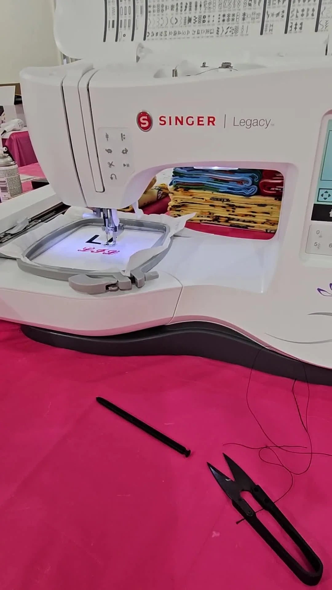 A wide-angle view of the Singer Legacy SE300 actively stitching a monogram in the hoop, with the Singer logo visible mid-project.