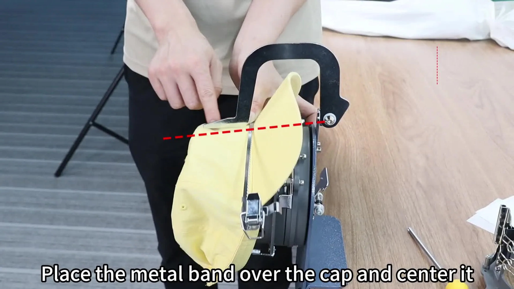 A yellow baseball cap is centered on the cap station with the alignment arm pulled down, showing the exact seam-to-notch alignment before latching.