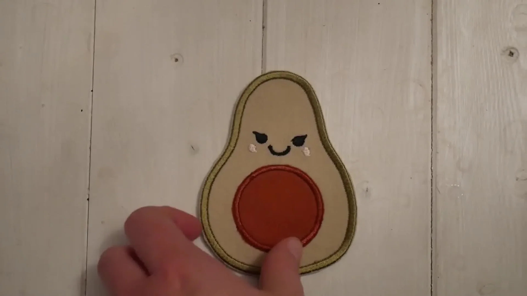 A close-up of a finished embroidered avocado patch held up to show clean edges and a professional, ready-to-press finish.