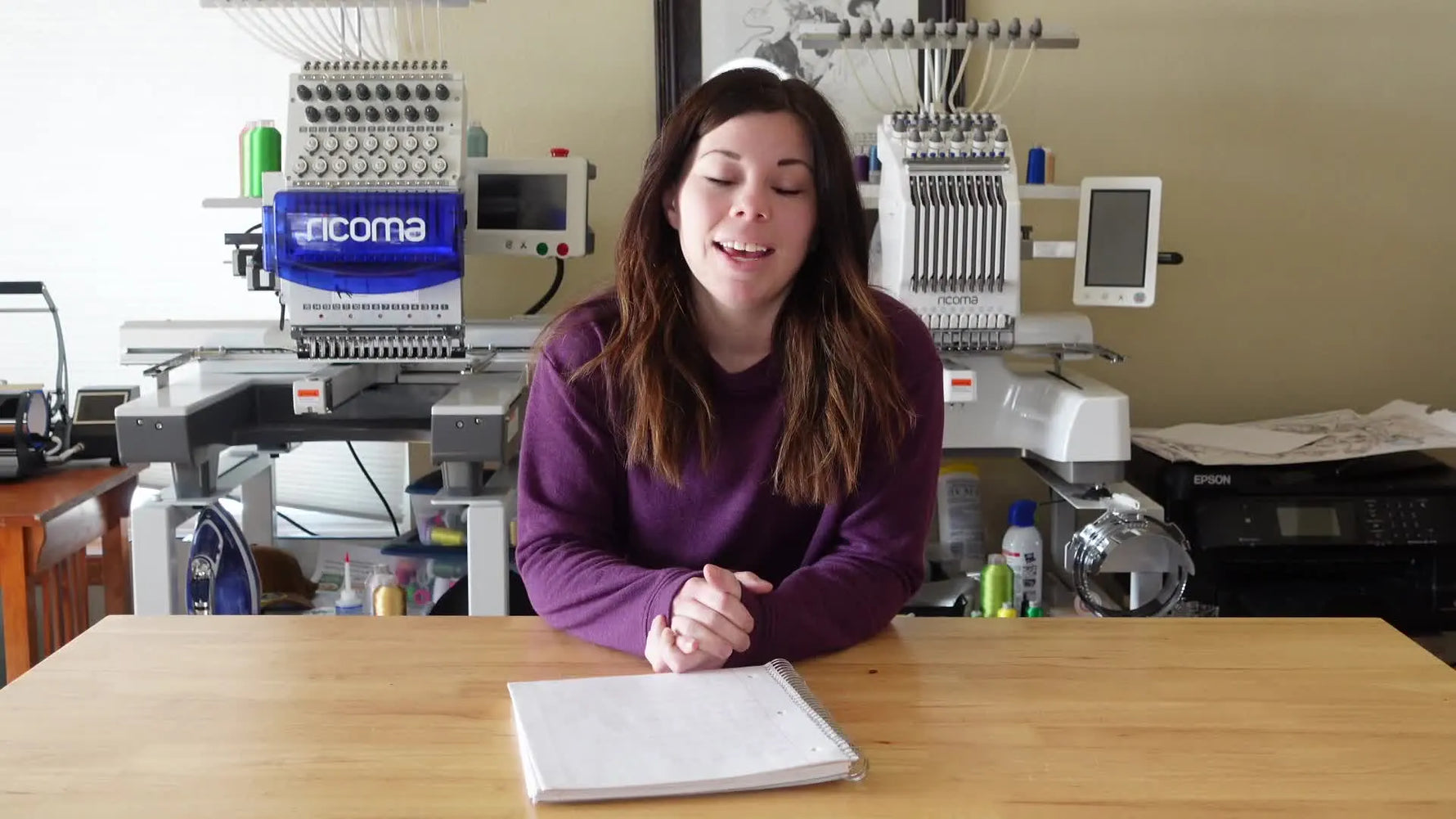 Kayla introducing her video on advertising local embroidery business, with two Ricoma multi-needle embroidery machines in the background.