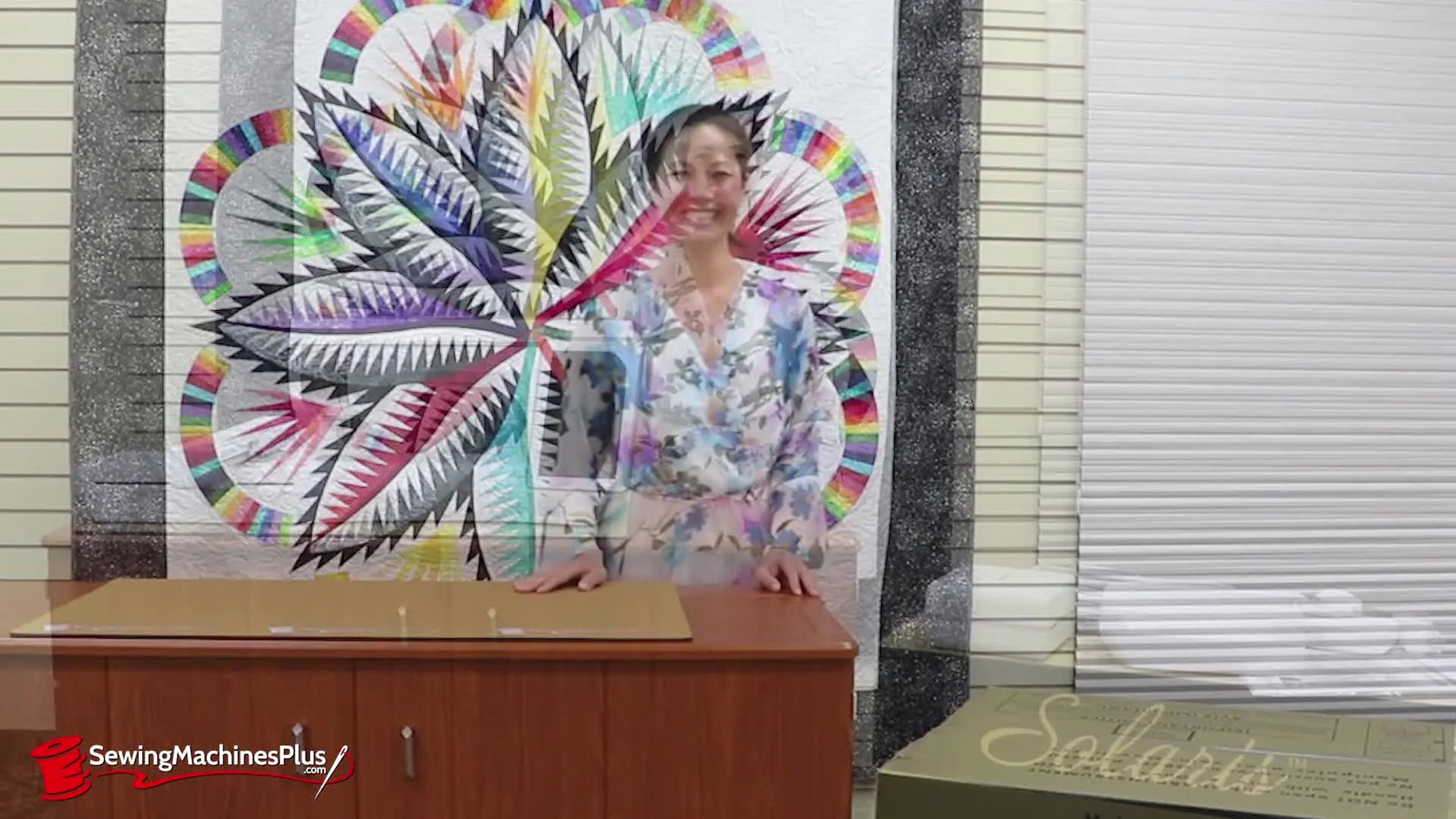 Denise Wild stands beside the unboxed Baby Lock Solaris with the embroidery unit and extension table attached, ready to demonstrate the included accessories.