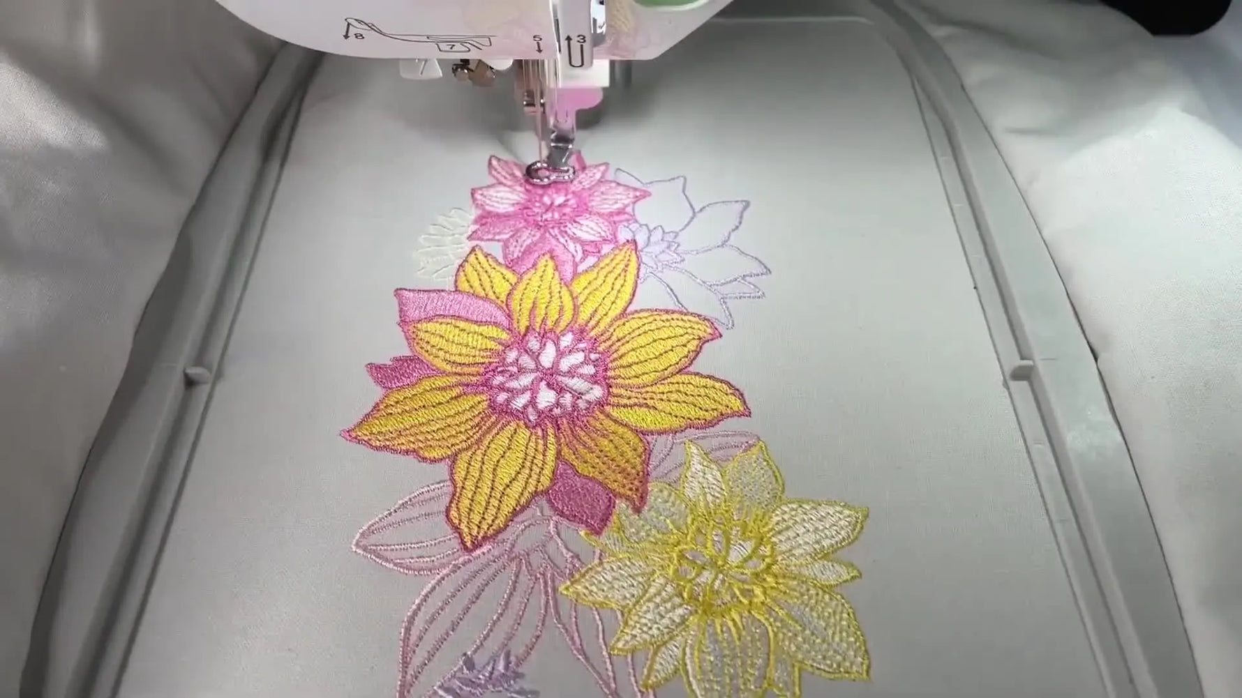 A close-up of the Brother NQ1700e stitching a multi-colored floral design on white fabric inside a hoop.