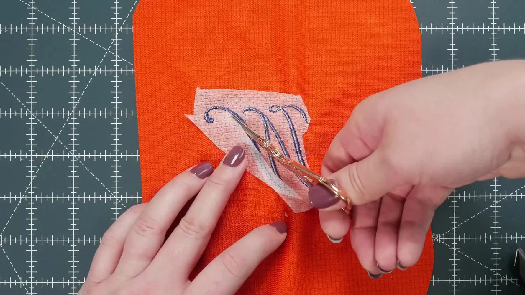 The back of a finished embroidery shows a clean Cut-Away stabilizer trim close to the stitch line for long-term support on knit fabric.