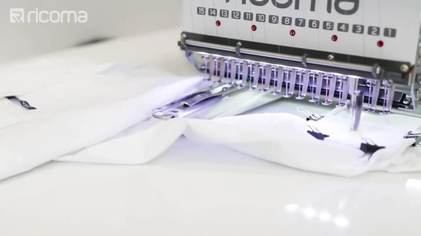 A close-up of a commercial multi-needle head stitching a logo onto a dress shirt cuff held in a specialized metal frame.