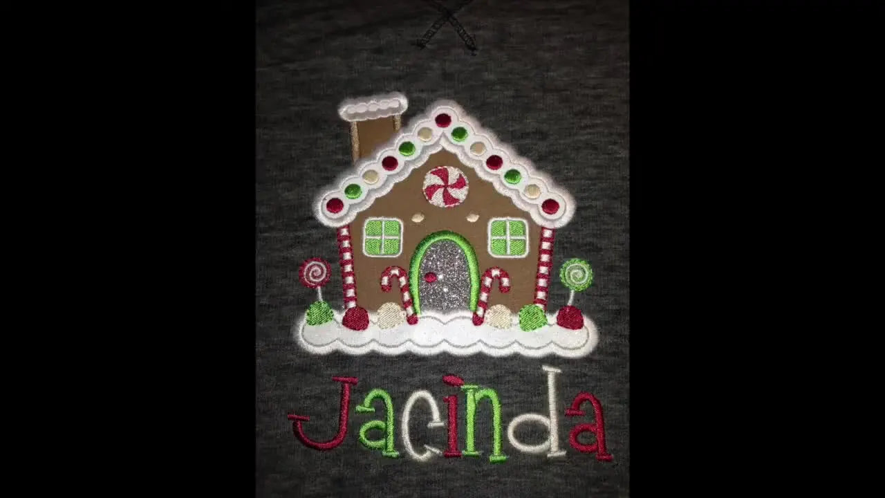 A finished gingerbread house appliqué on a grey garment shows flat, gap-free glitter HTV edges and clean satin stitch coverage.