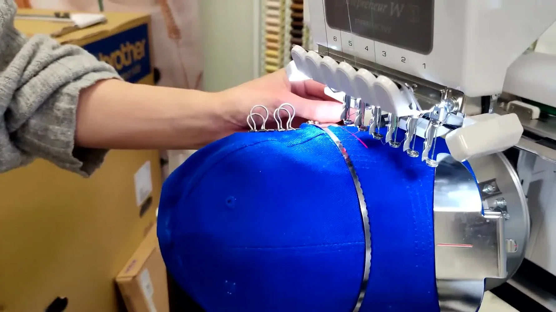 A framed baseball cap is rotated sideways to safely pass under the embroidery head before snapping into the cap driver.