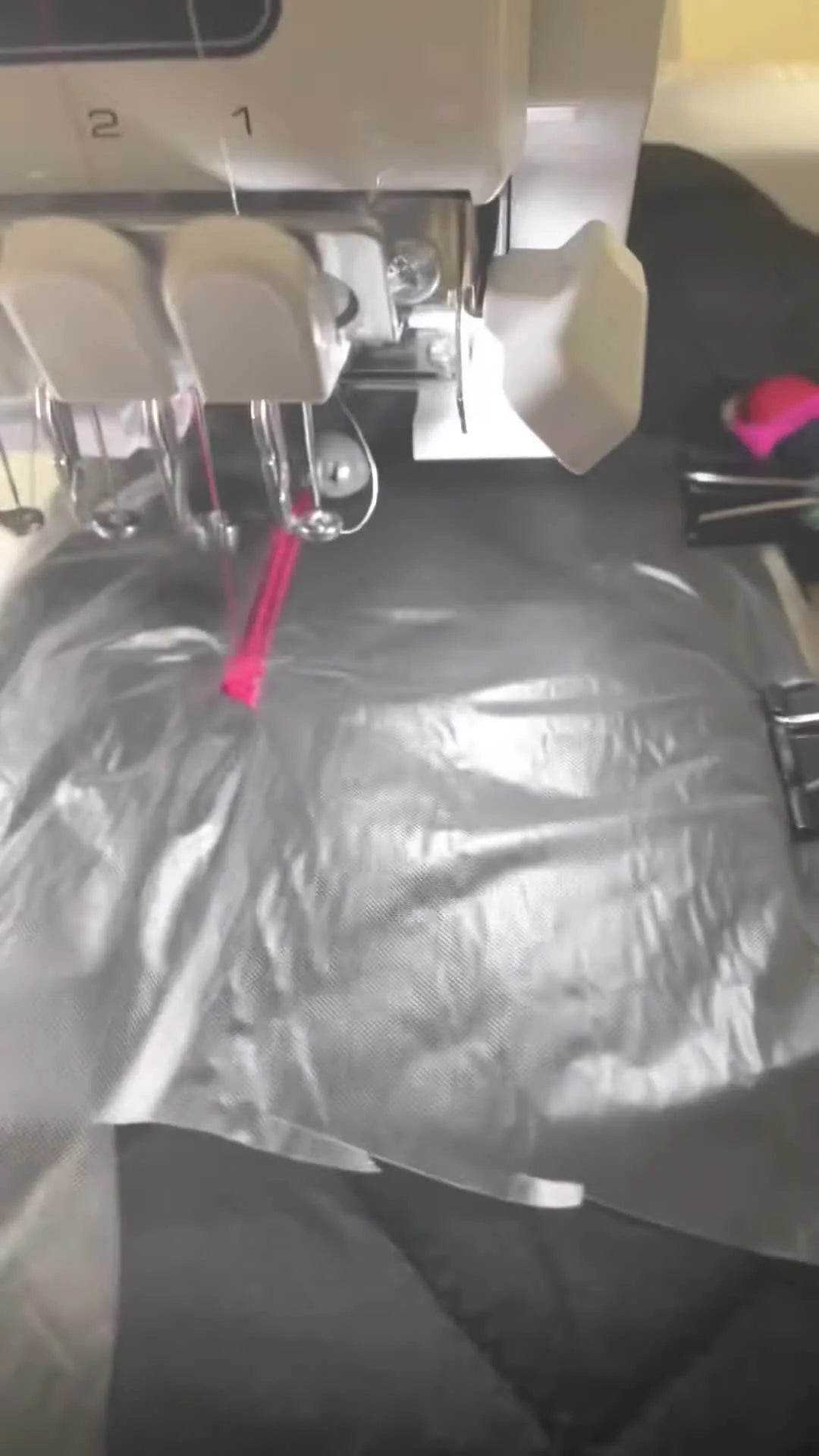 A close-up action shot shows the needle stitching a pink monogram through water-soluble topping on a quilted vest.