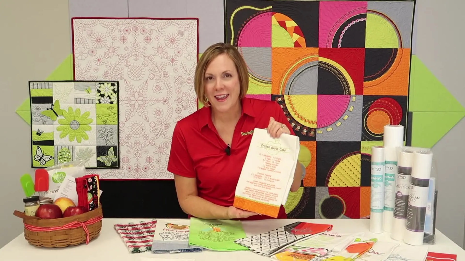 A finished white tea towel shows a red embroidered recipe with a bright orange fabric border, held up for a clear look at layout and legibility.