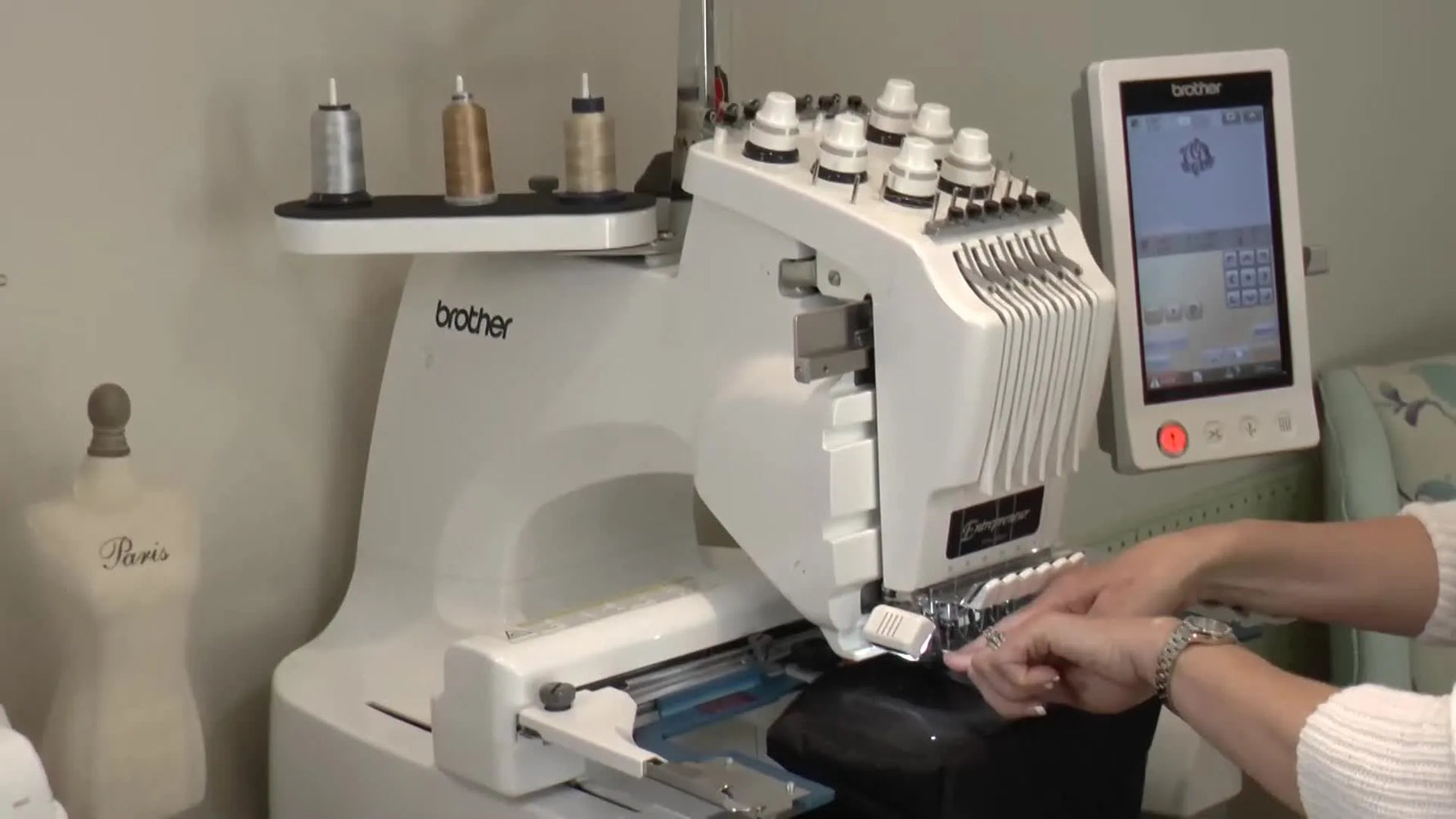 A close-up shows the needle bar being pulled down by hand to confirm the needle point lands exactly on the center-marking pin before stitching.