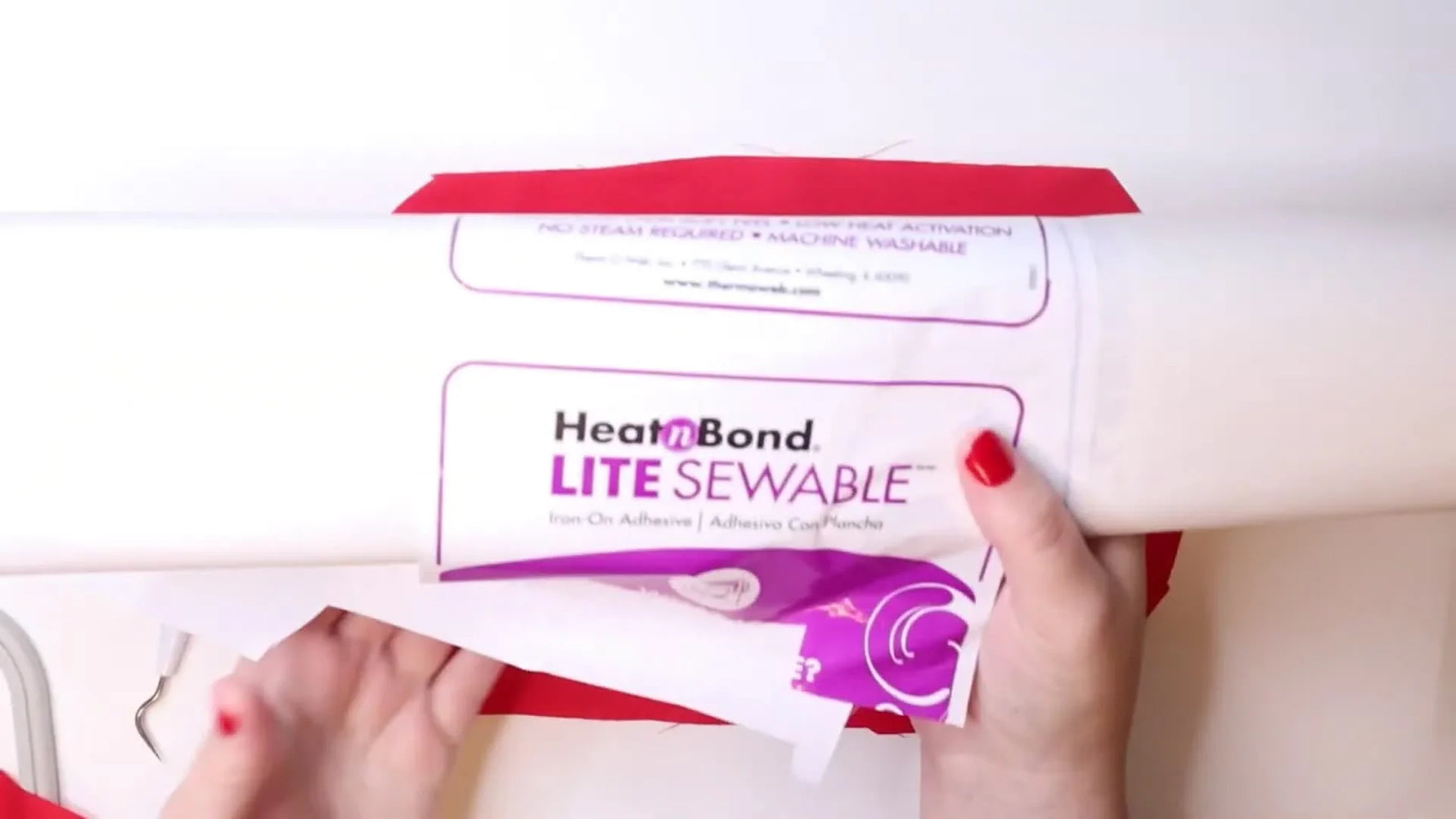 A Brother PE800 stitches a white heart outline and name onto red fabric that’s been floated on sticky tear-away stabilizer.