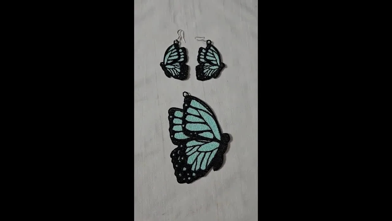 Finished aqua-and-black FSL butterfly earrings and a matching pendant laid out after the water-soluble stabilizer has been washed away.