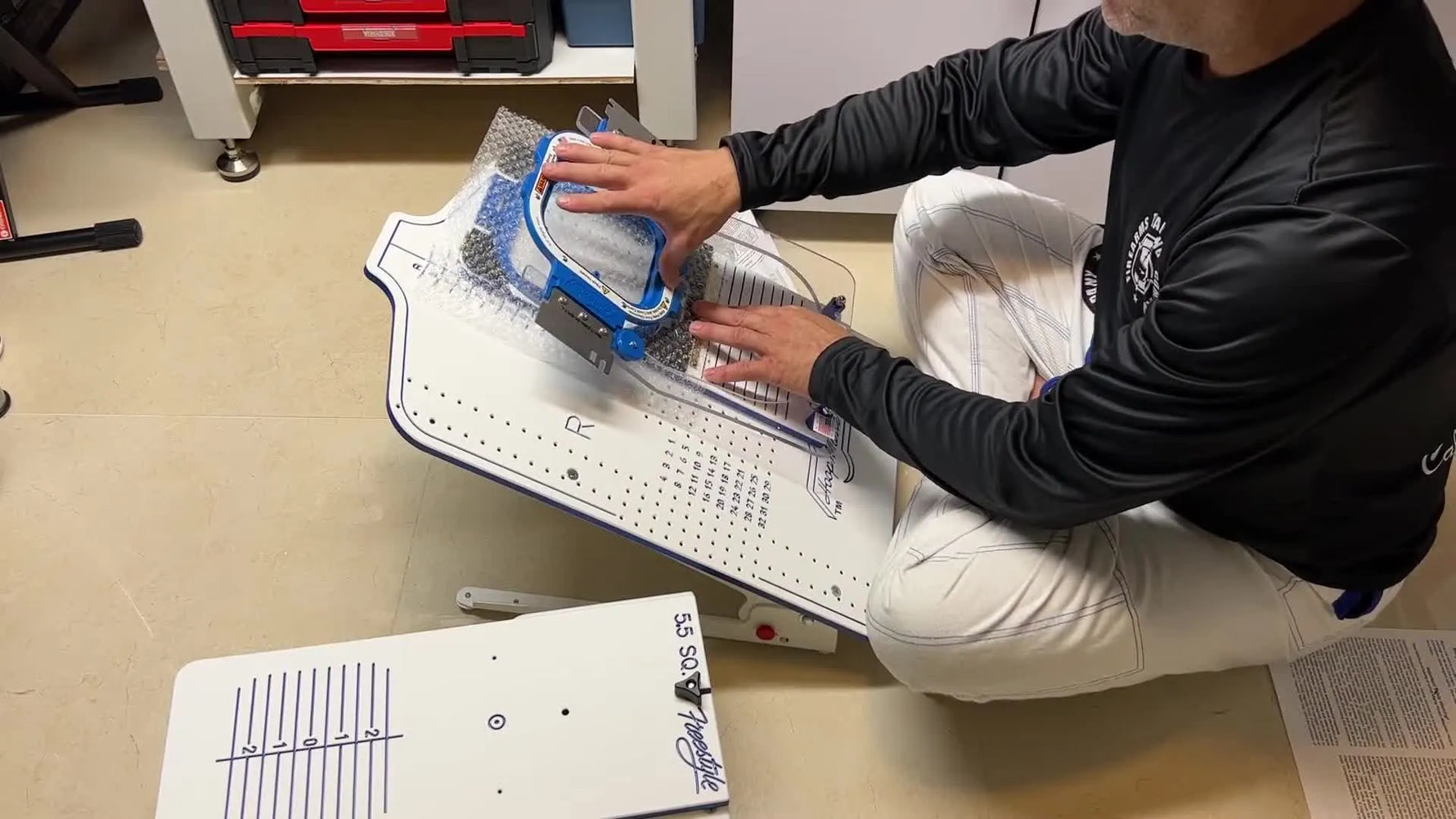 A magnetic top hoop is about to be pressed onto a garment on the HoopMaster fixture, capturing the exact moment that creates fast, repeatable hooping tension.