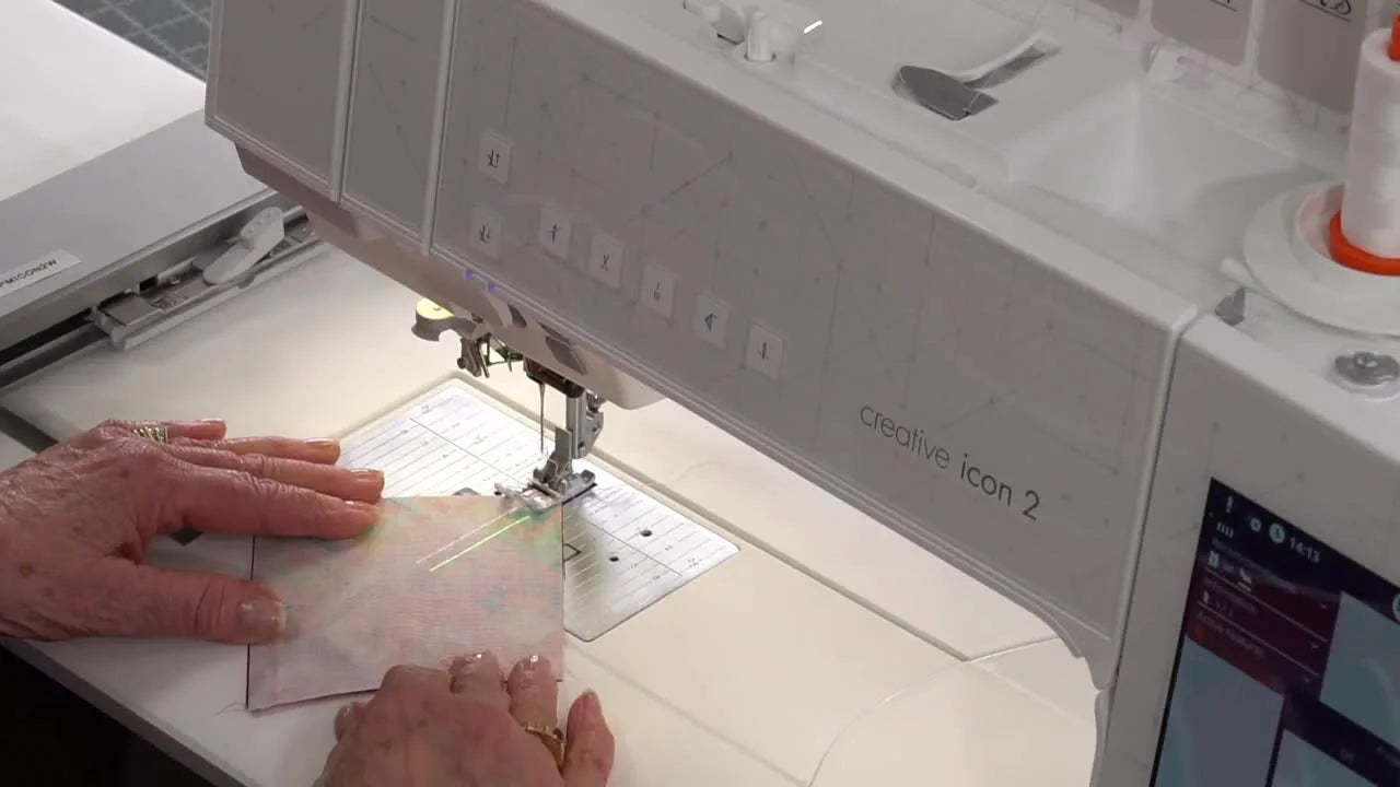 A close-up, top-down view of fabric being stitched while the Pfaff Creative Icon 2 projects red and green alignment guides onto the fabric.