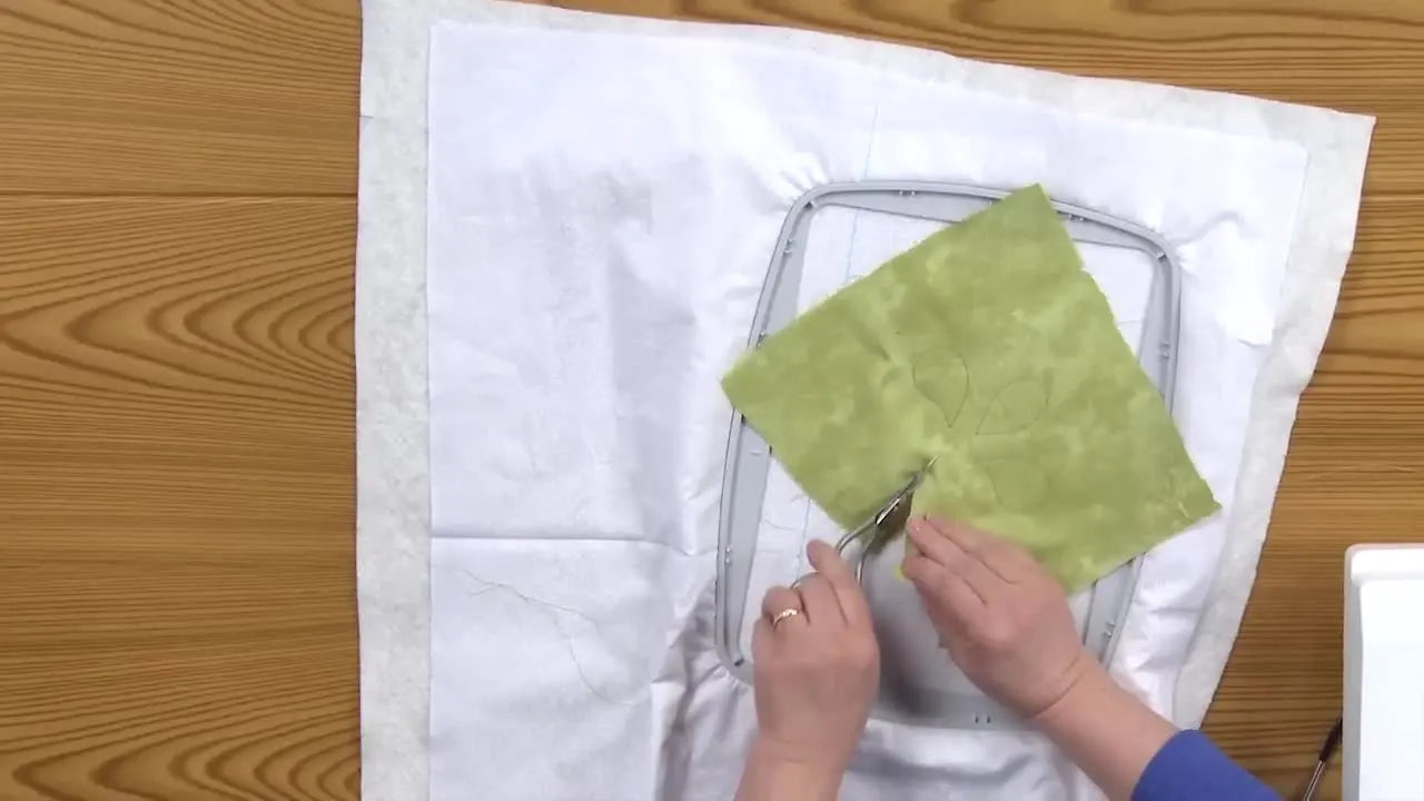 Overhead view of duckbill appliqué scissors trimming green fabric close to the tack-down stitching for a clean satin-finished edge.
