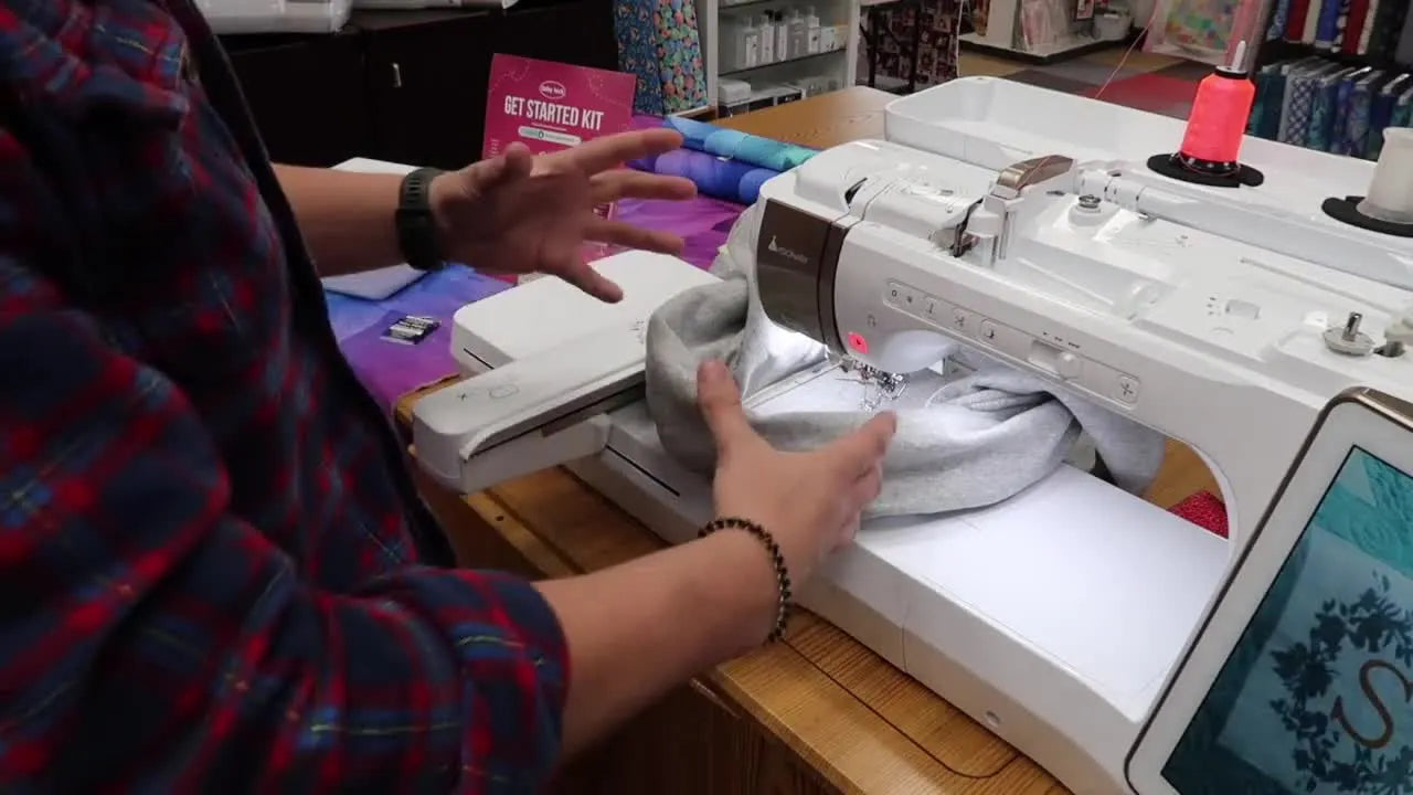 A hooped sweatshirt sits around the embroidery machine head in a “bowl” shape so only the front layer is under the needle.