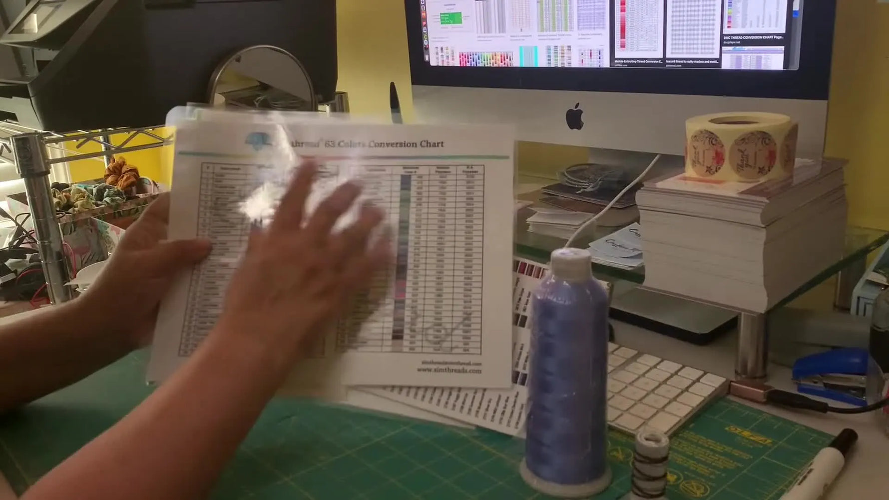A close-up of a finger tracing a row on a laminated thread conversion chart to confirm an exact color match.