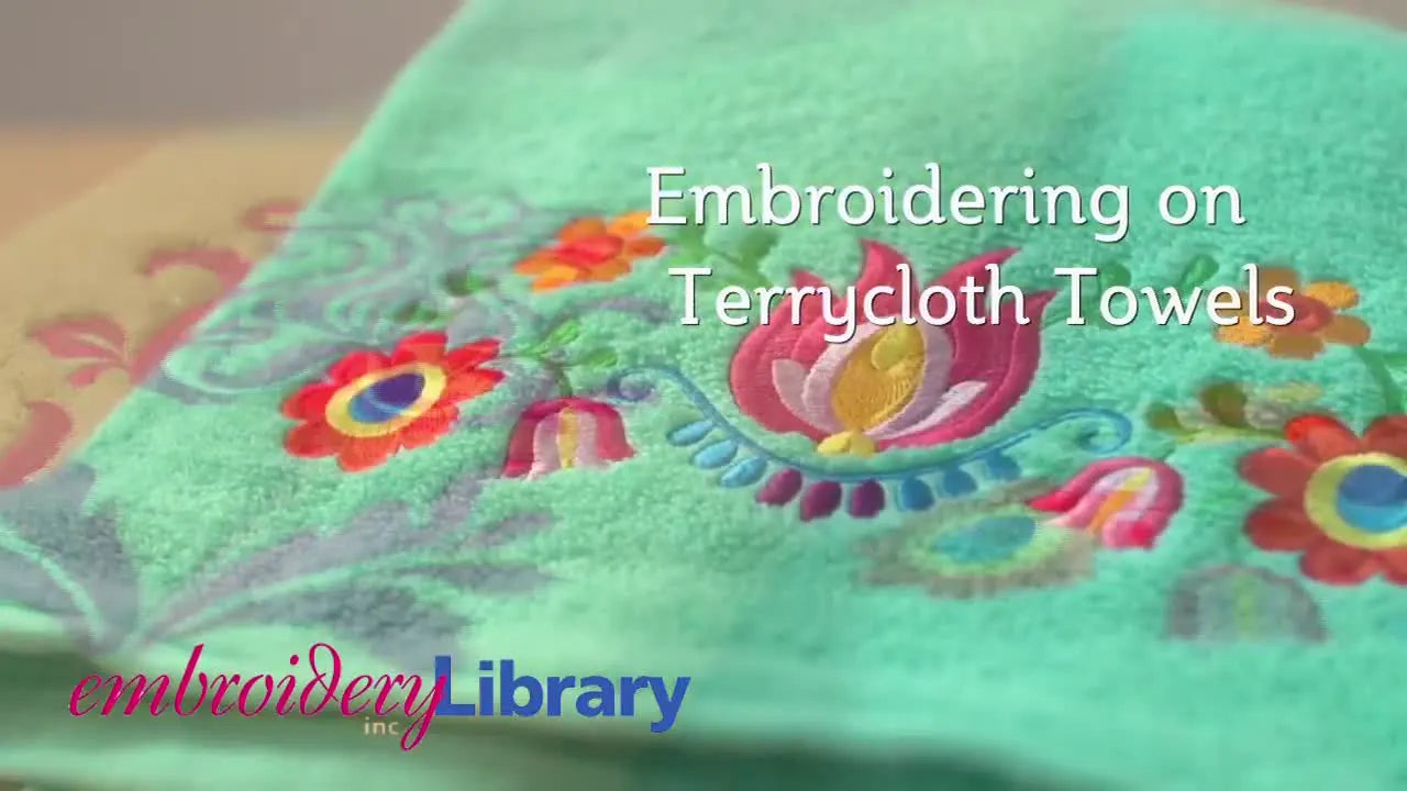 A close-up of a terrycloth towel showing a vibrant floral embroidery design sitting cleanly on the towel’s textured loops.