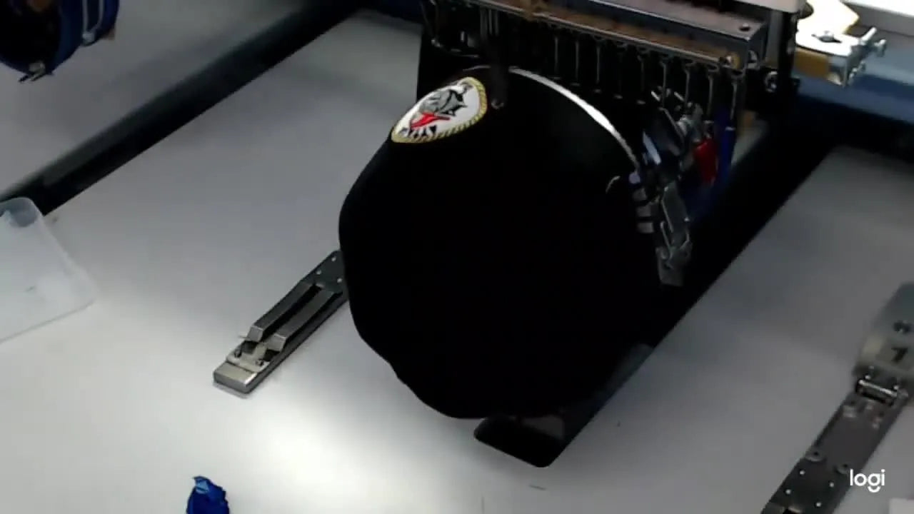 The presenter holds a finished black New Era cap with a perfectly applied circular patch that looks like it was embroidered directly onto the hat.