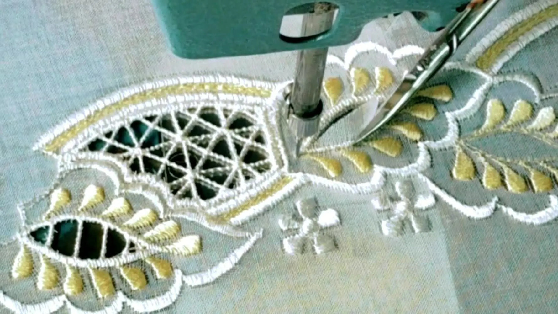 Machine embroidering a complex cutwork design with white and gold threads, with scissors poised