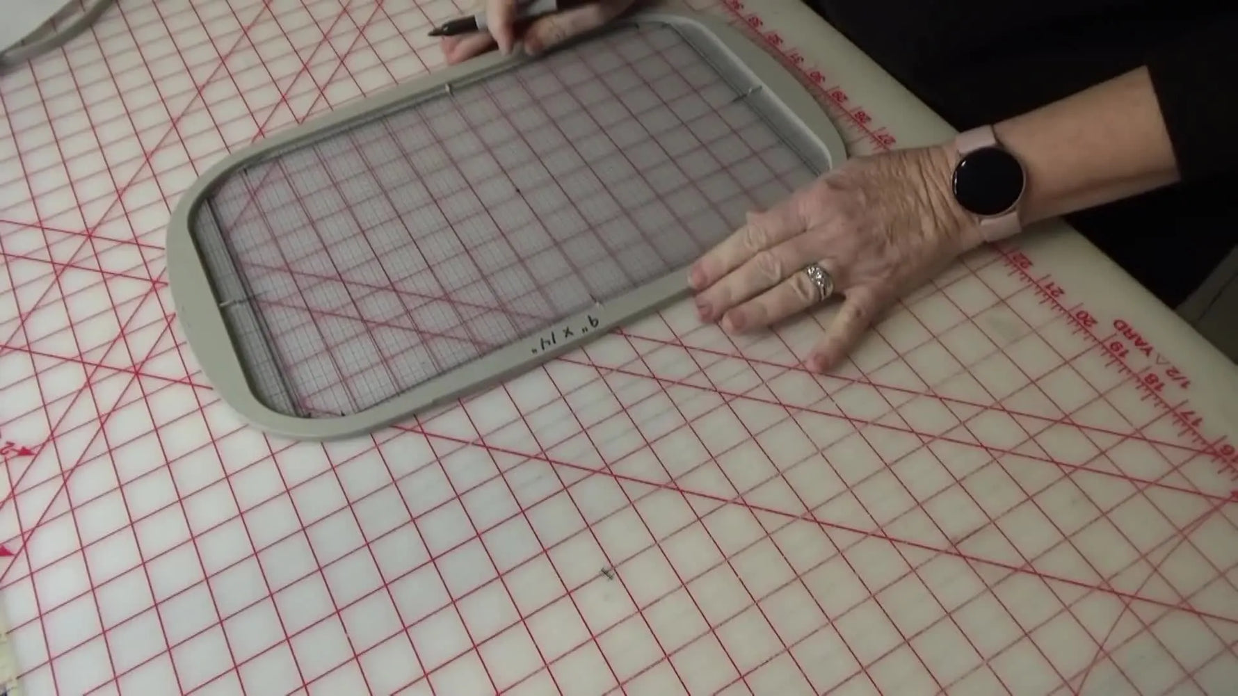 An overhead close-up shows an eyelet punch creating a clean center needle hole in a DIY grid insert for a Brother 9x14 embroidery hoop.