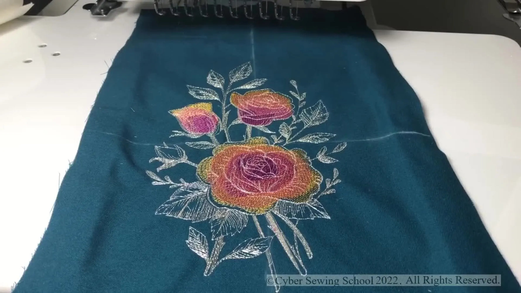 An overhead view of the finished rose embroidery stitched on teal fabric, showing the final color palette and contrast.