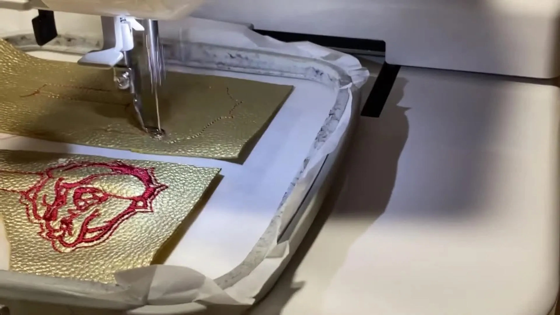 A close-up of the Janome 230E stitching the maroon bulldog outline onto gold faux leather inside the 5.5 x 5.5 hoop.