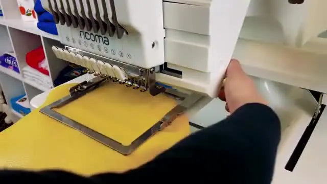 A close-up of a hand pressing the clamp lever down to lock a pleather clutch flap securely in place for embroidery.