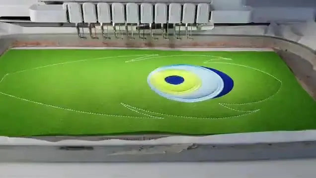 Close-up of the multi-needle machine stitching the colorful satin-stitch “eye” detail on a peacock feather component in the hoop.