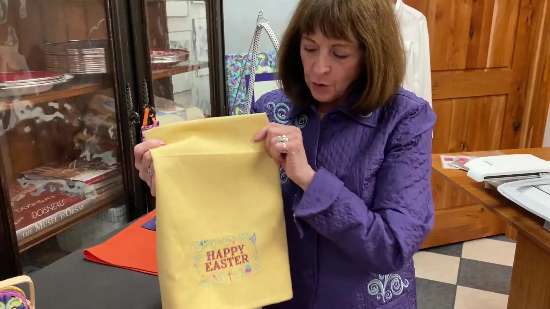A finished yellow towel is held up to show a crisp “Happy Easter” embroidery result after proper stabilizing, hooping, and design orientation.