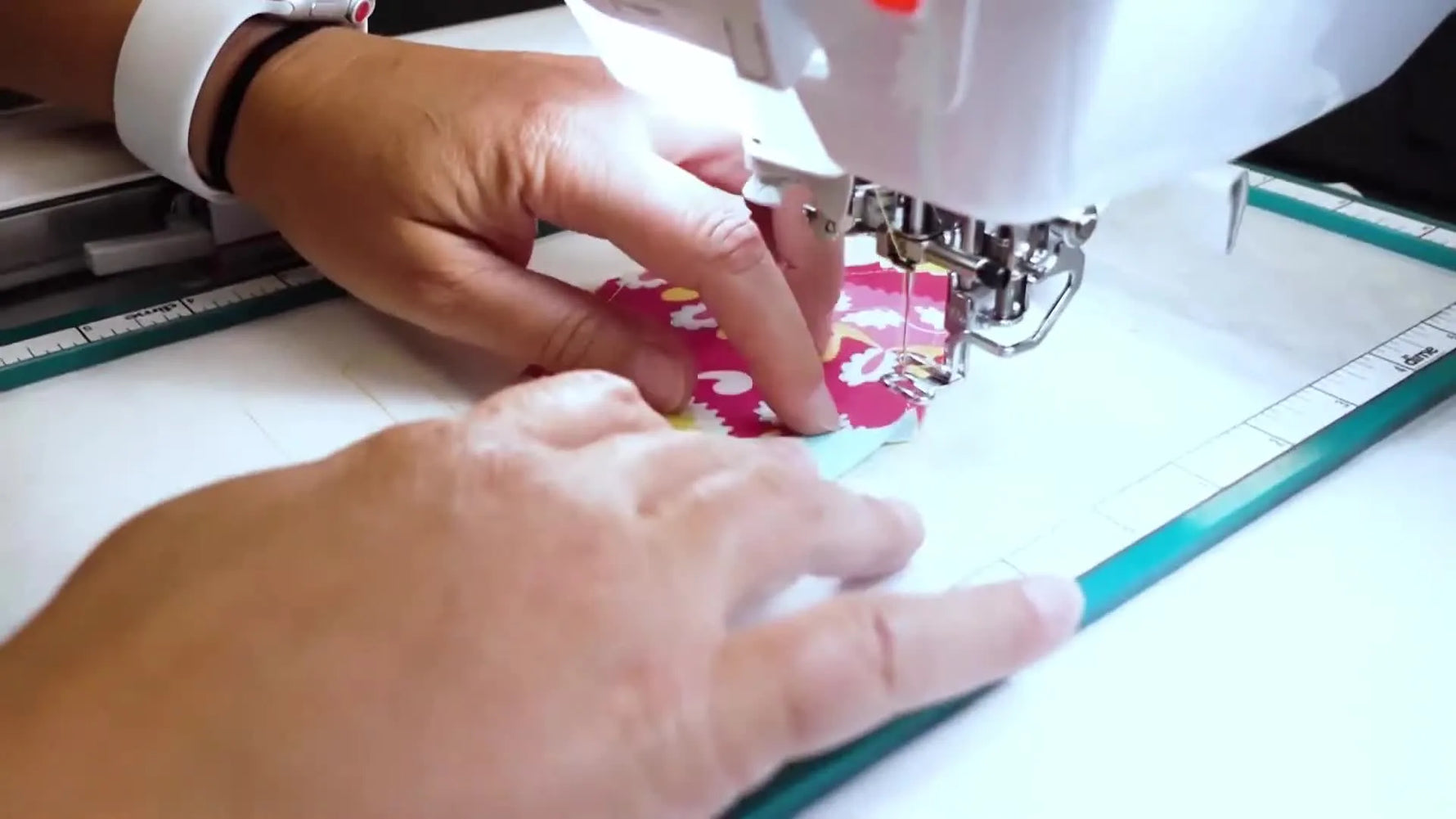 Hands flip the second fabric piece open and finger-press the seam flat inside the embroidery hoop during an in-the-hoop quilt block stitch-out.
