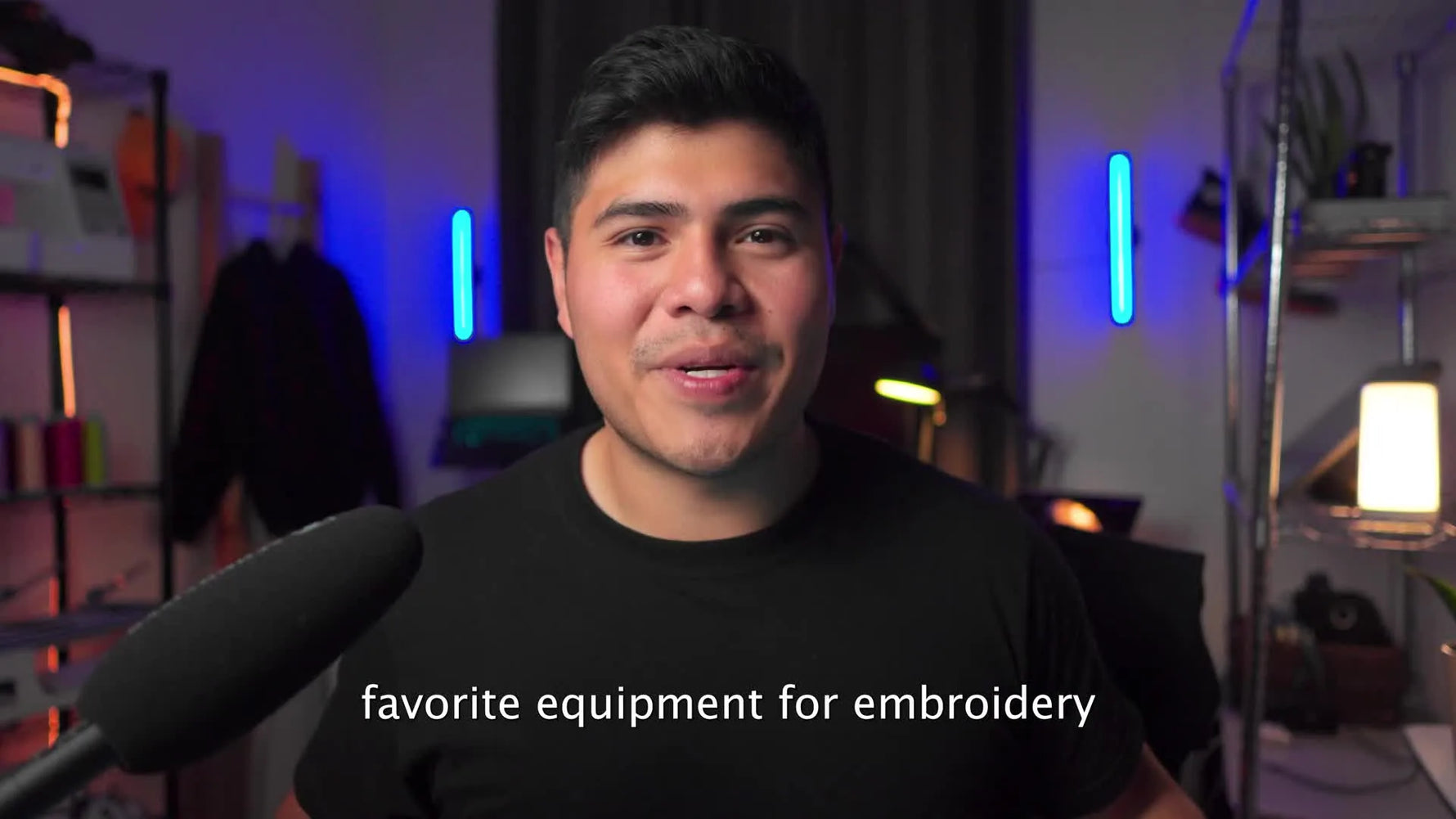 The presenter holds up a magnetic embroidery hoop to show the fastest, lowest-stress way to clamp fabric without leaving shiny hoop marks.