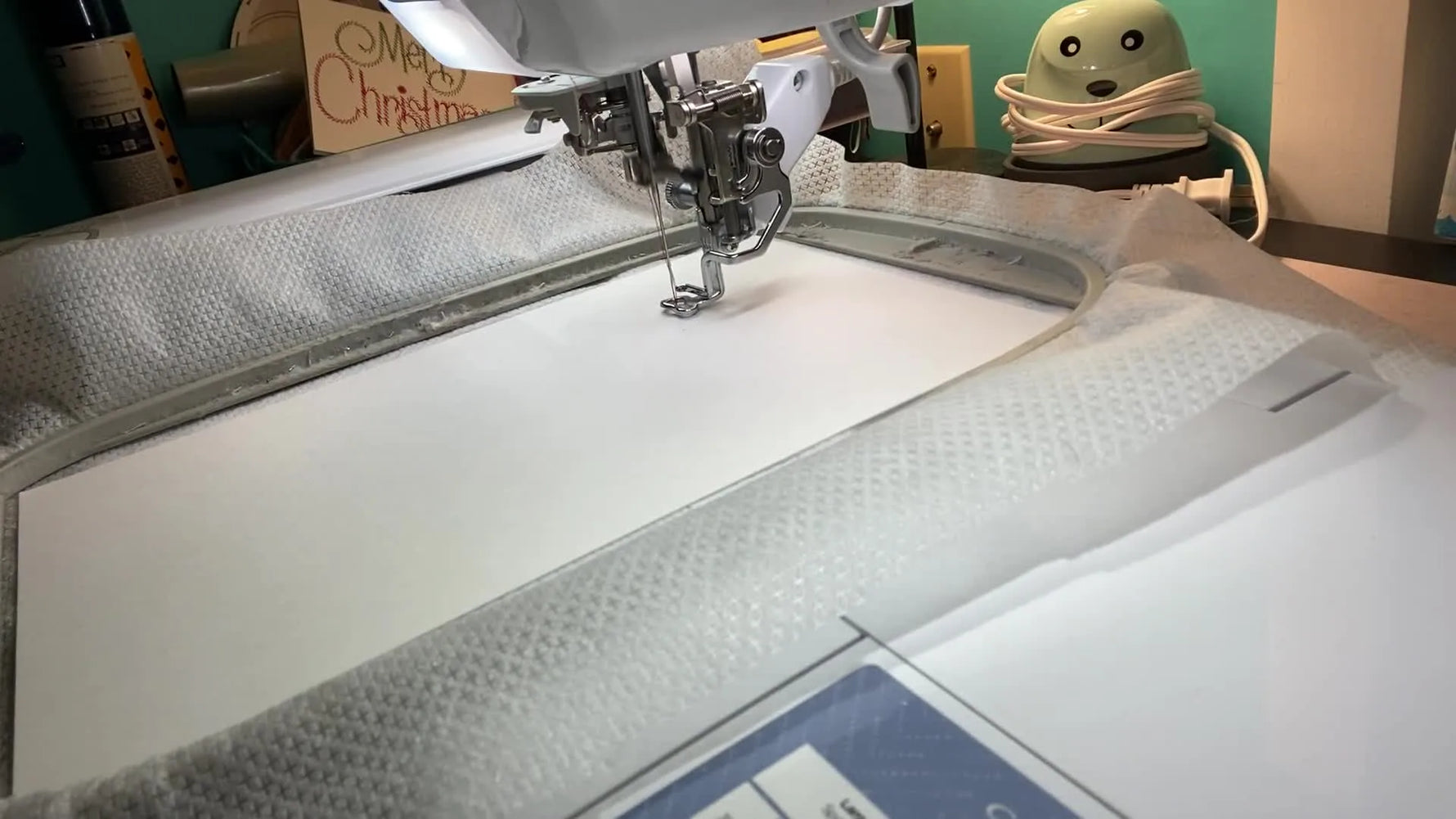 A close-up action shot of the needle stitching red lettering onto white cardstock inside a 5x7 hoop.