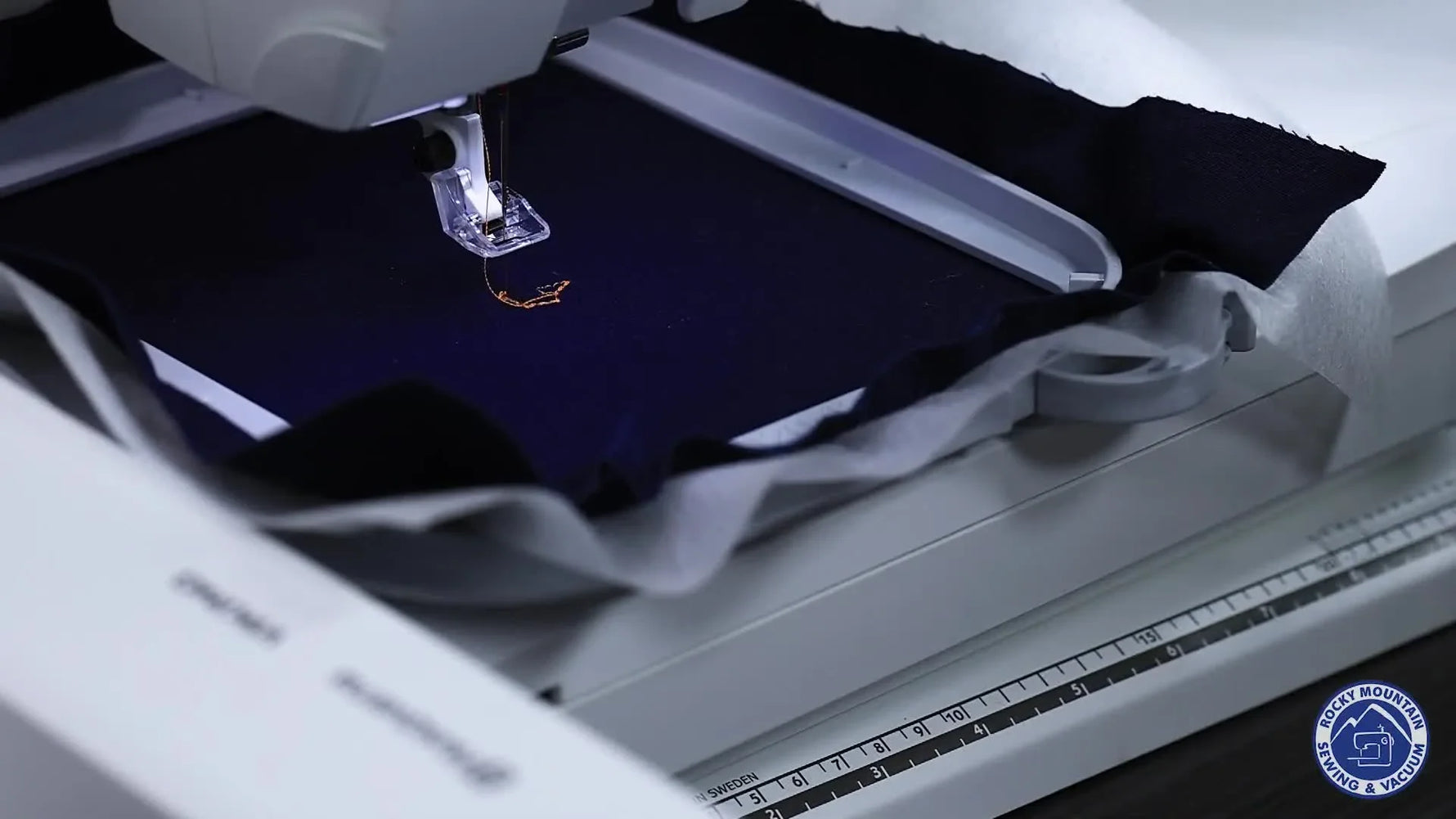 A close-up of the Husqvarna Viking Designer Topaz 50 actively stitching an orange spider design on dark blue fabric.