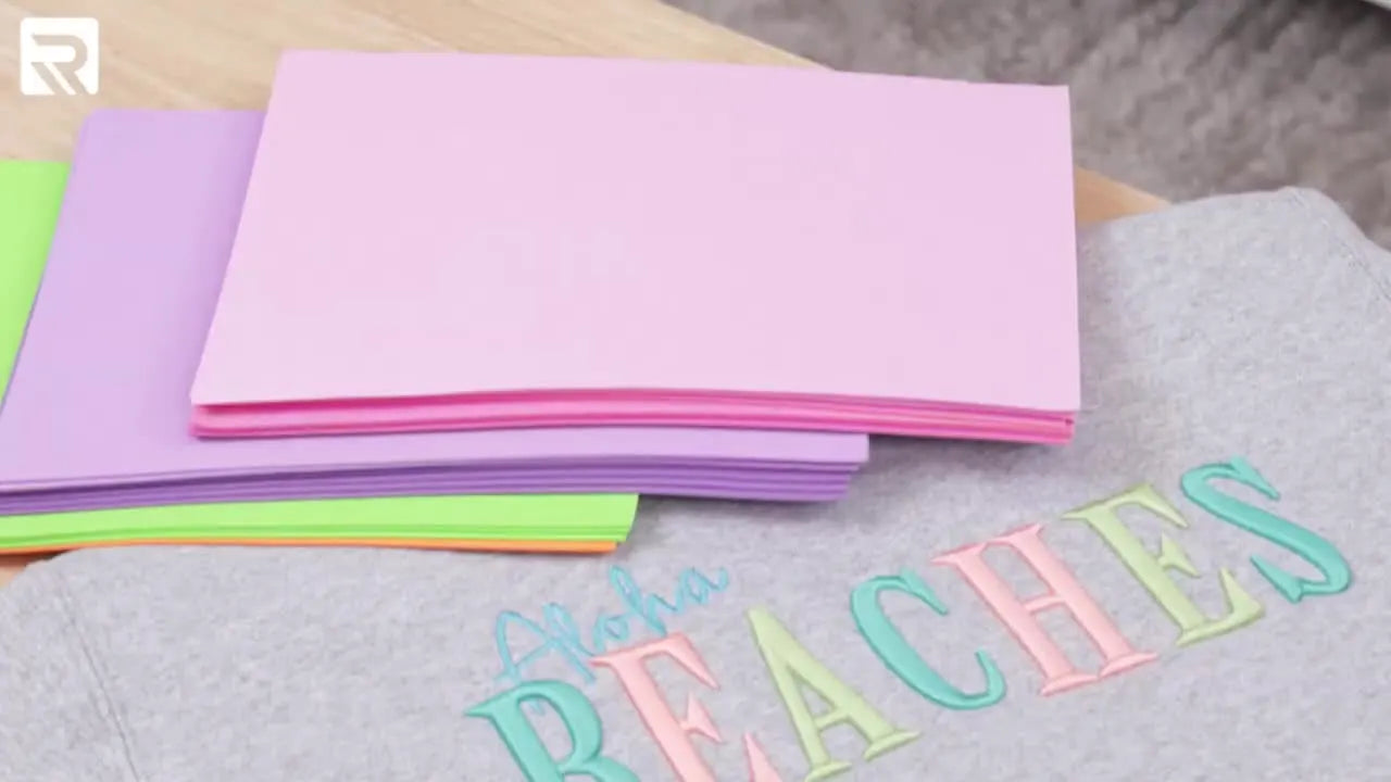 Janet holds up the finished grey sweatshirt featuring a colorful 3D puff foam “Aloha BEACHES” embroidery design.