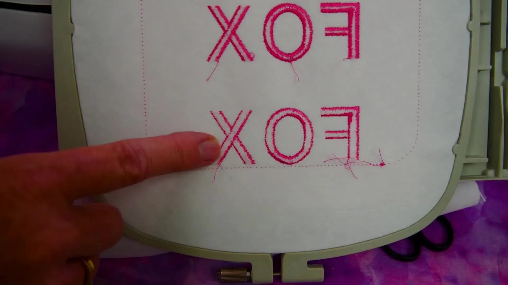A close-up of the back of the stitched “FOX” sample where the presenter points out what correct and incorrect tension look like.