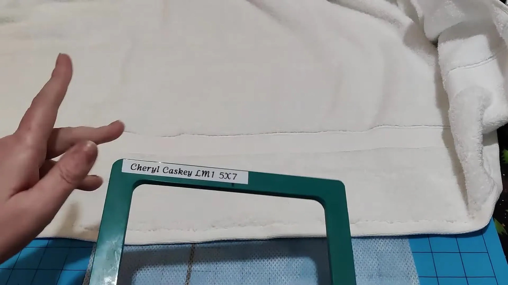 A close-up shows a magnetic top frame snapping down over a thick towel, demonstrating the fastest way to clamp bulky terry cloth securely.