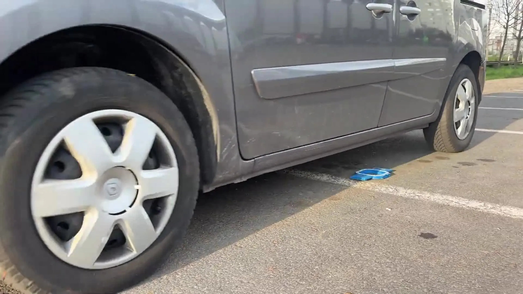 A car tire drives over a blue magnetic embroidery hoop on asphalt during an extreme durability test.