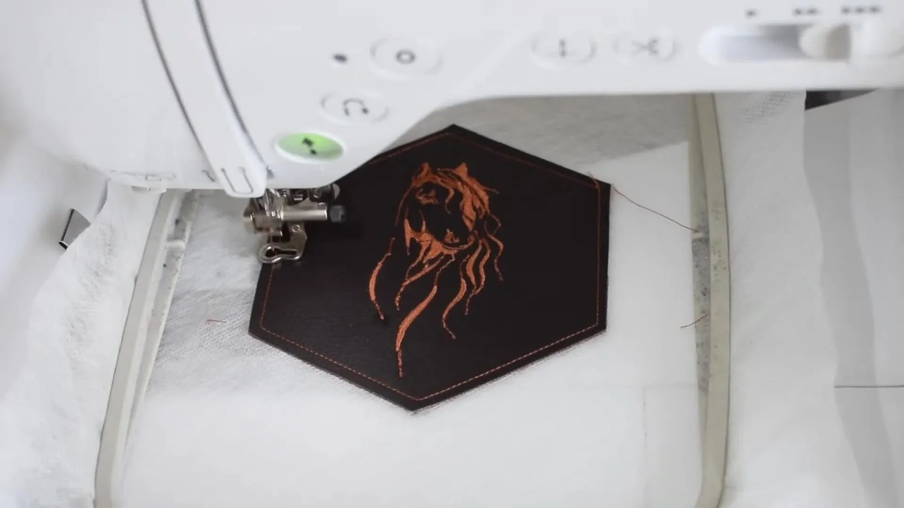 Close-up of the embroidery machine stitching the final satin border around the hexagon coaster, locking the top and backing layers together.