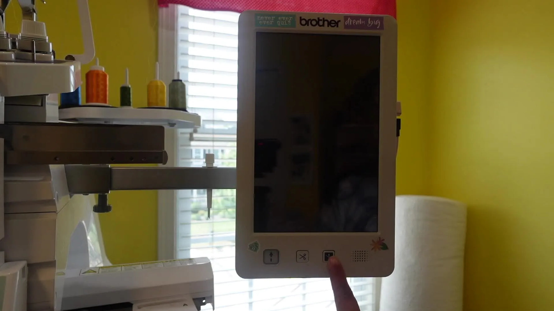 A close-up of a finger holding the PR1055X automatic needle threader button while powering on to enter firmware update mode.