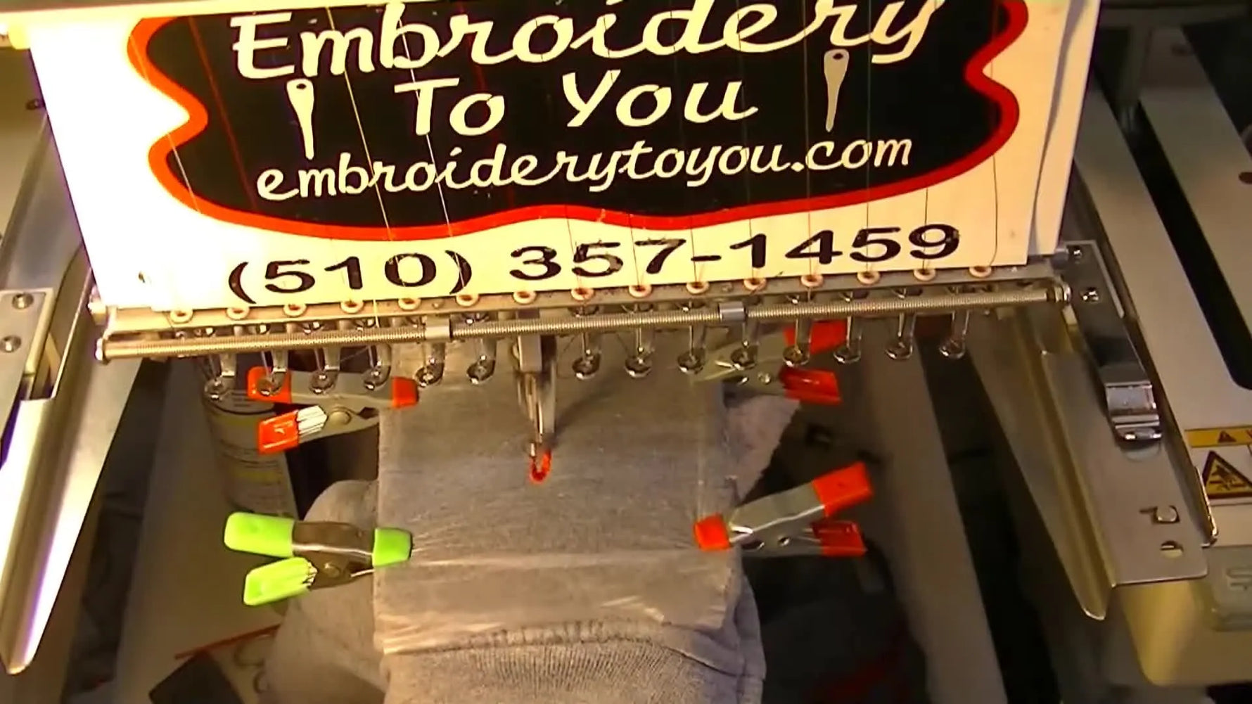 A zippered hoodie pocket is mounted on a multi-needle embroidery machine using a Fast Frames sash frame with spring clamps holding water-soluble topping in place.