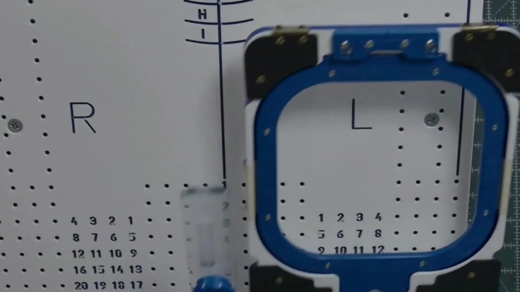 A blue-and-white magnetic hoop sits docked on a white placement station board, ready for repeatable alignment.