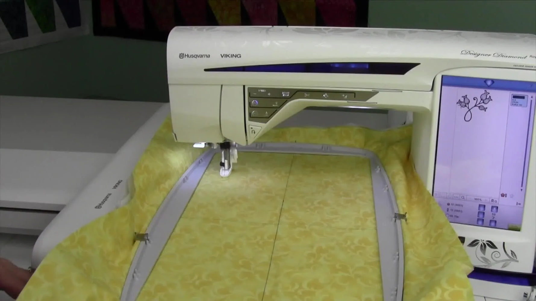 The machine actively stitching a blue floral motif on yellow fabric.