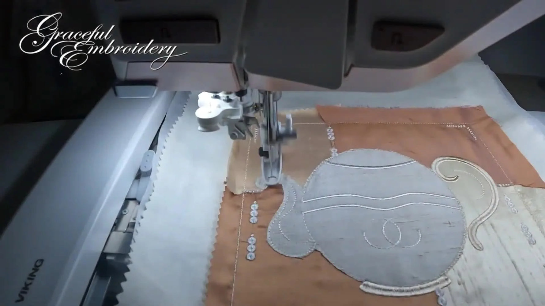 A close-up of the machine forming a dense satin stitch border around the teapot handle area.