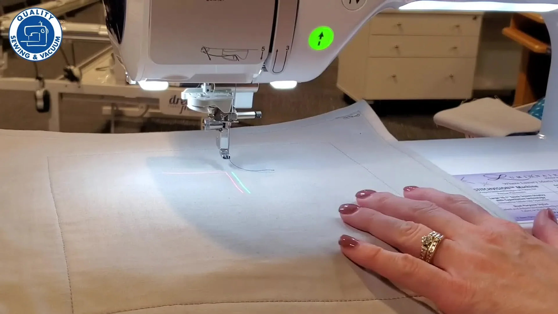 A close-up of the Brother Luminaire projector displaying a blue decorative stitch directly on the fabric for real-size preview and adjustment.